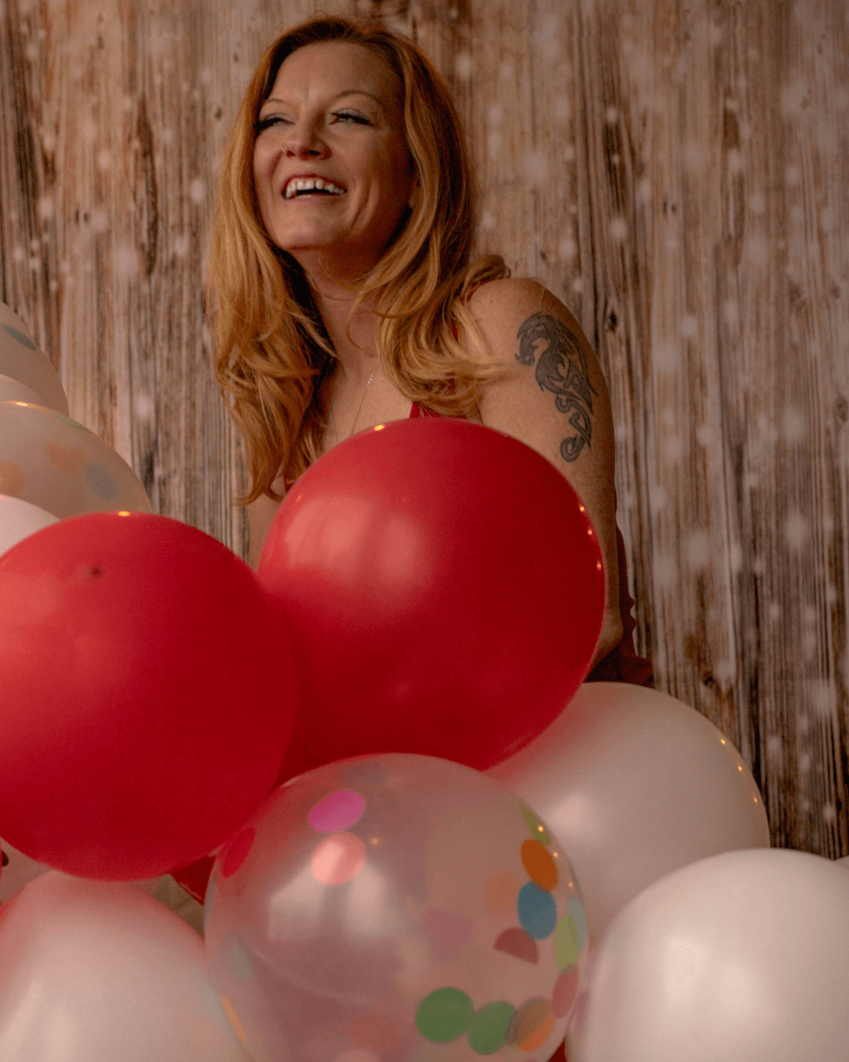 Woman in front of a wooden bokeh background smiling and 
surrounded by balloons